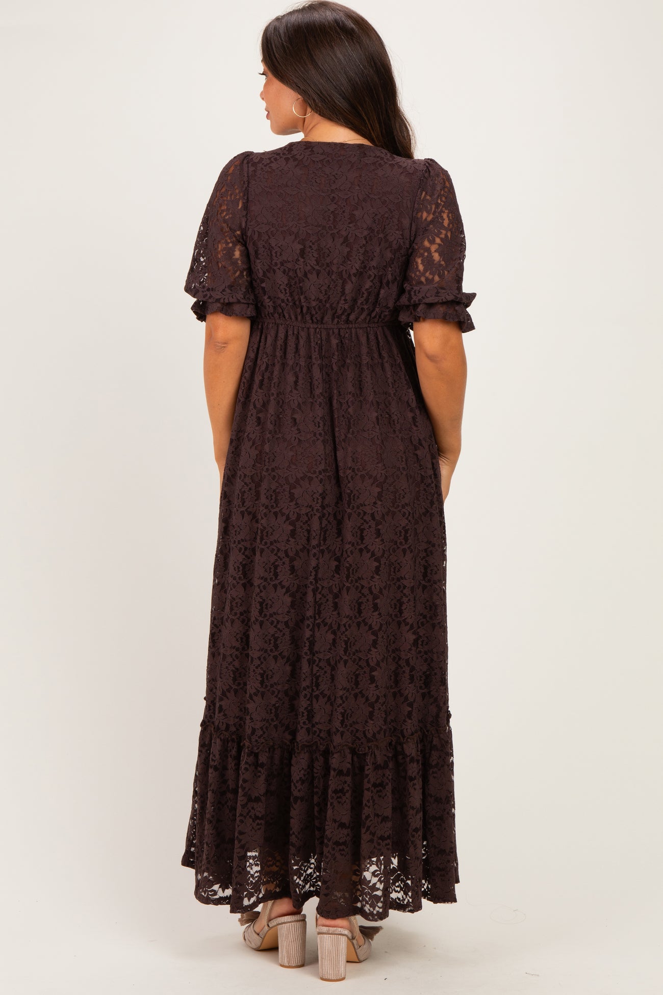 woman wearing a dark brown lace maternity maxi dress with short sleeves and a fitted waist, showing her baby bump from behind