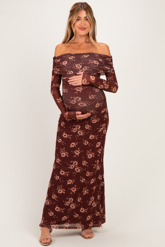 woman wearing a burgundy floral off-shoulder maternity dress with long sleeves and holding her baby bump