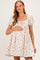 woman wearing a beige floral maternity dress with puff sleeves and holding her baby bump