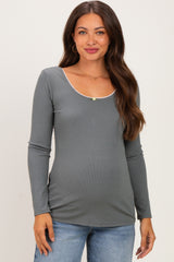 woman wearing a gray long sleeve maternity top with a scoop neckline and decorative stitching, showing her baby bump