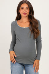 woman wearing a gray long sleeve maternity top with a scoop neckline and decorative trim, showing her baby bump