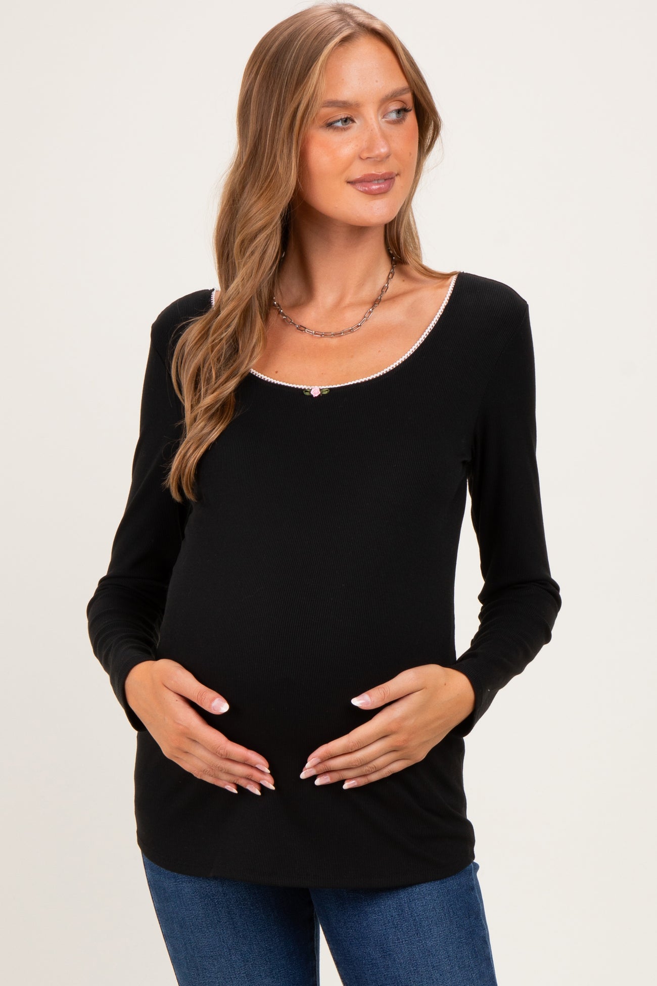 woman wearing a black long sleeve maternity top with a scoop neckline and holding her baby bump