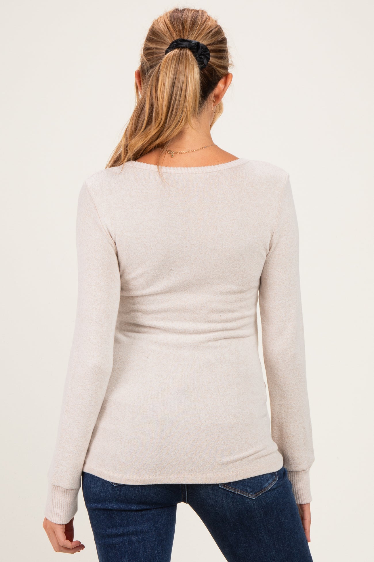 woman wearing a light beige long sleeve maternity top, back view, paired with dark blue jeans