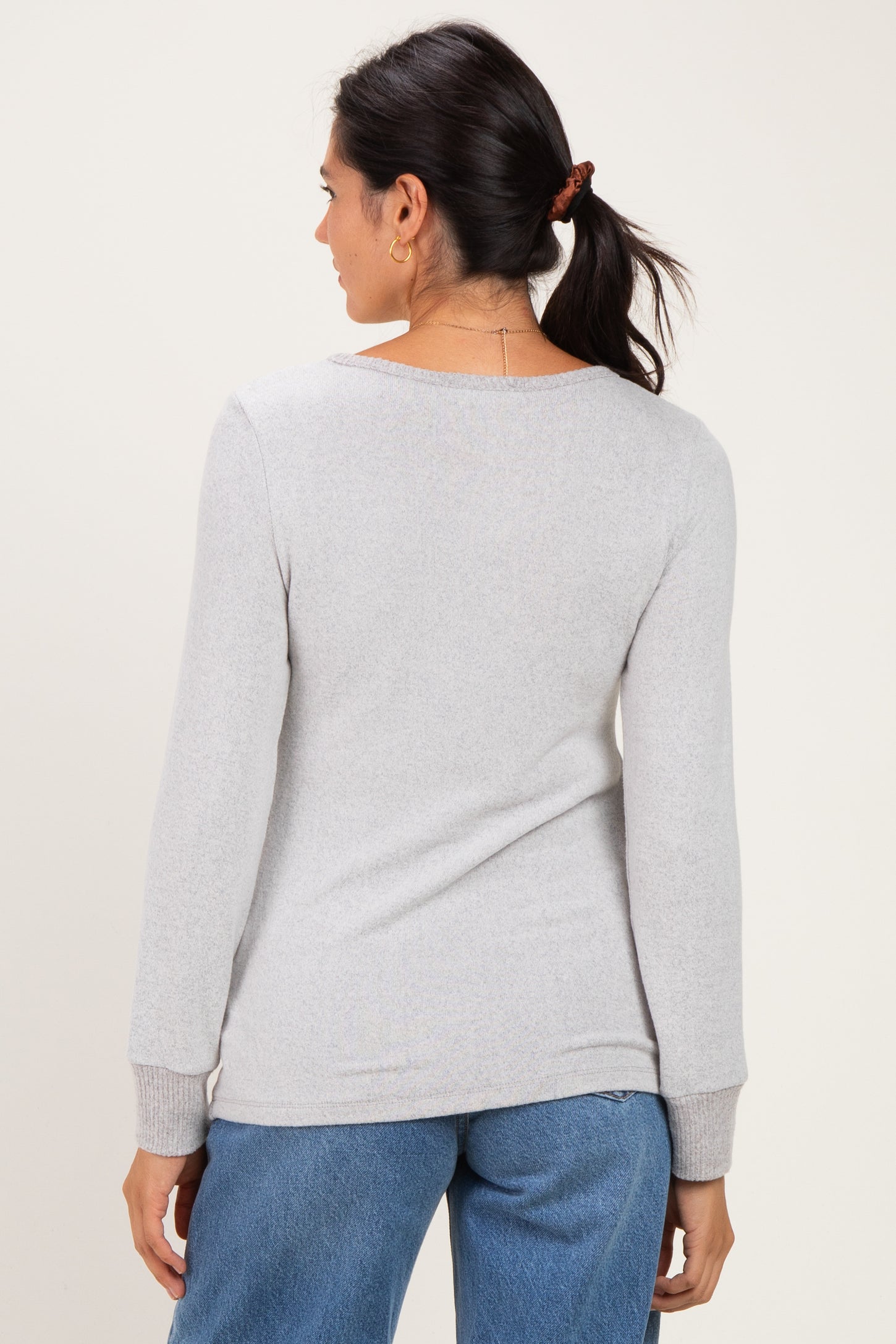 woman wearing a light gray long sleeve sweater, viewed from the back, paired with blue jeans