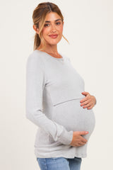 woman wearing a light gray maternity long sleeve top and cradling her baby bump