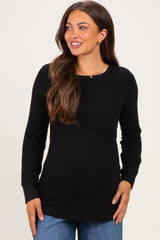 woman wearing a black long sleeve maternity top with a fitted bodice and relaxed hemline, smiling
