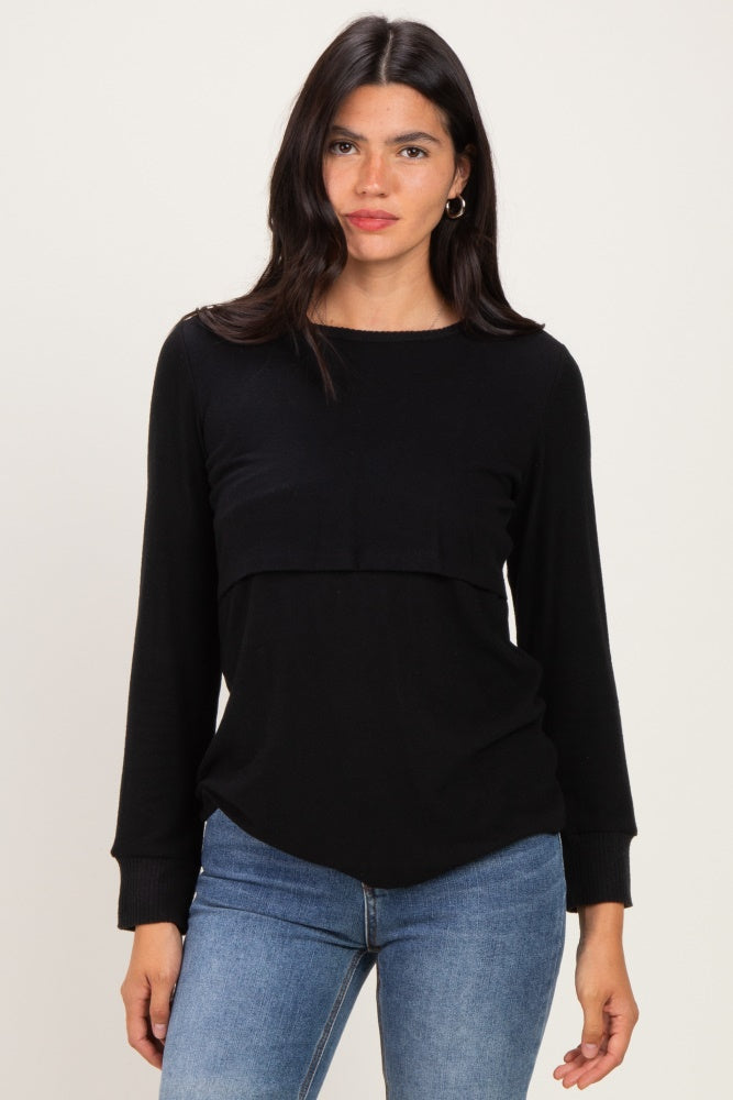 woman wearing a black long sleeve top with a layered design and relaxed fit, paired with blue jeans