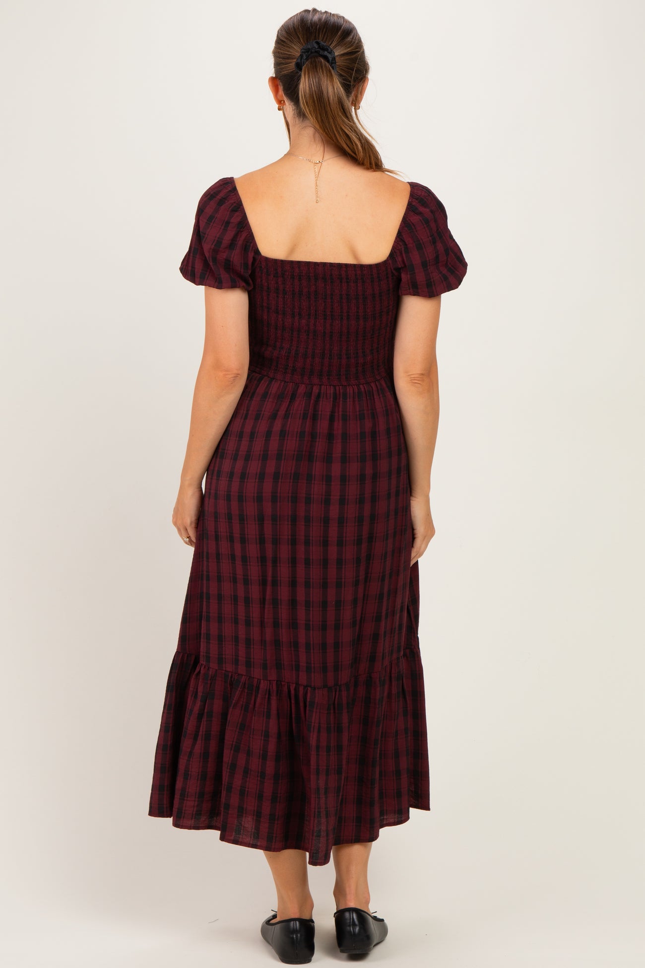 woman wearing a burgundy and black plaid maternity dress with puff sleeves and a ruffled hemline, seen from the back