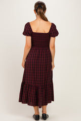 woman wearing a burgundy and black plaid maternity dress with puff sleeves and a ruffled hemline, seen from the back