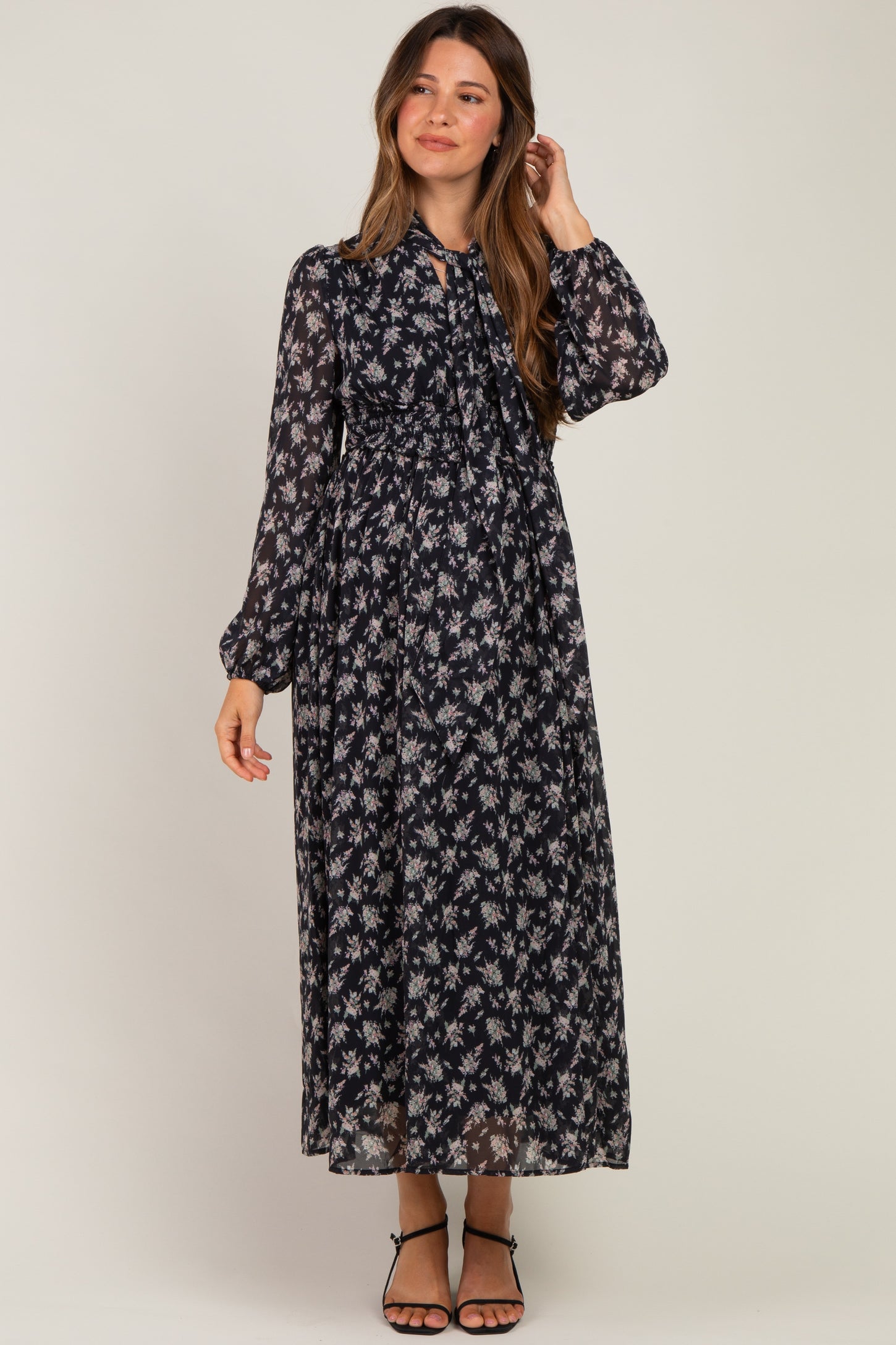 woman wearing a floral black maternity maxi dress with long sleeves and a tied neckline, showing her baby bump