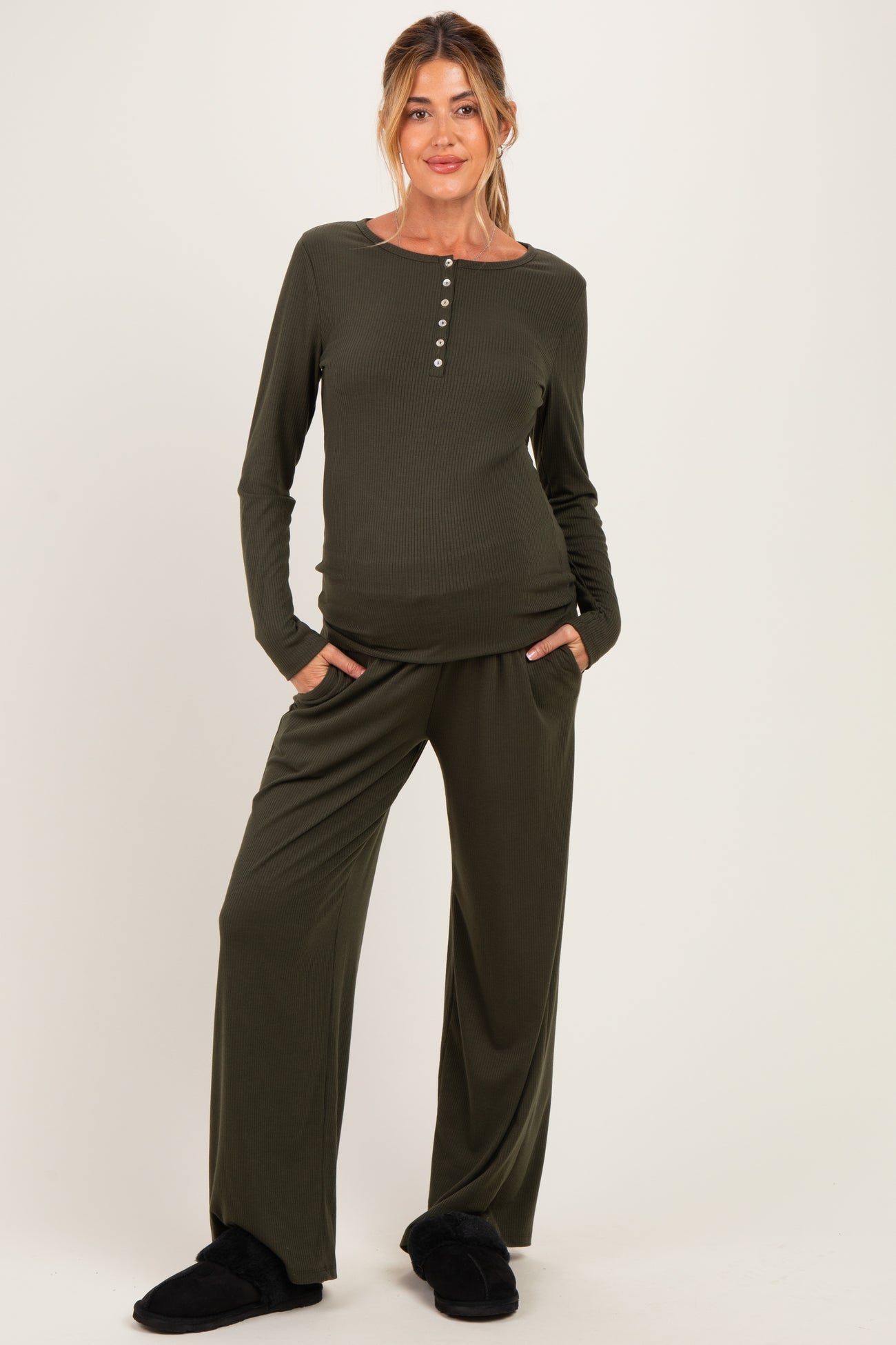 woman wearing a dark olive green maternity loungewear set with long sleeves and flared pants, hands in pockets, baby bump visible