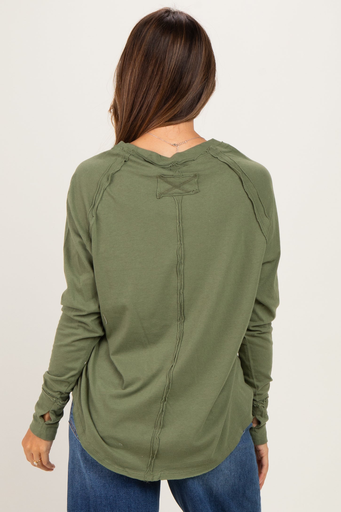 woman wearing an olive green long sleeve maternity top with distressed detailing and a relaxed fit