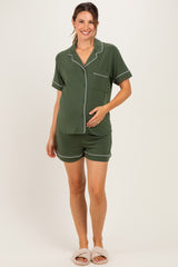 woman wearing a green maternity pajama set with shorts and a button-up top, gently cradling her baby bump