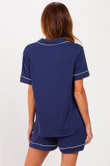 woman wearing a navy blue short sleeve pajama set with white piping, showing the back view