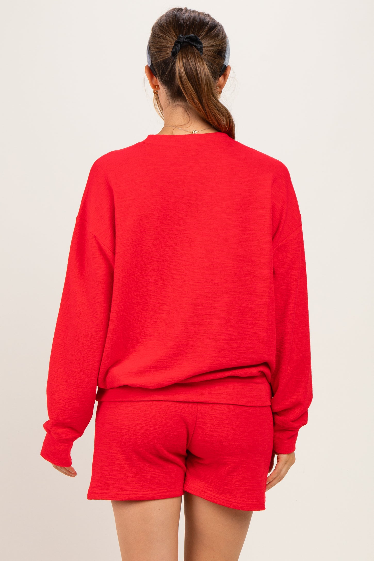 woman wearing a red maternity sweatshirt and matching shorts, showing her back with a comfortable, casual style