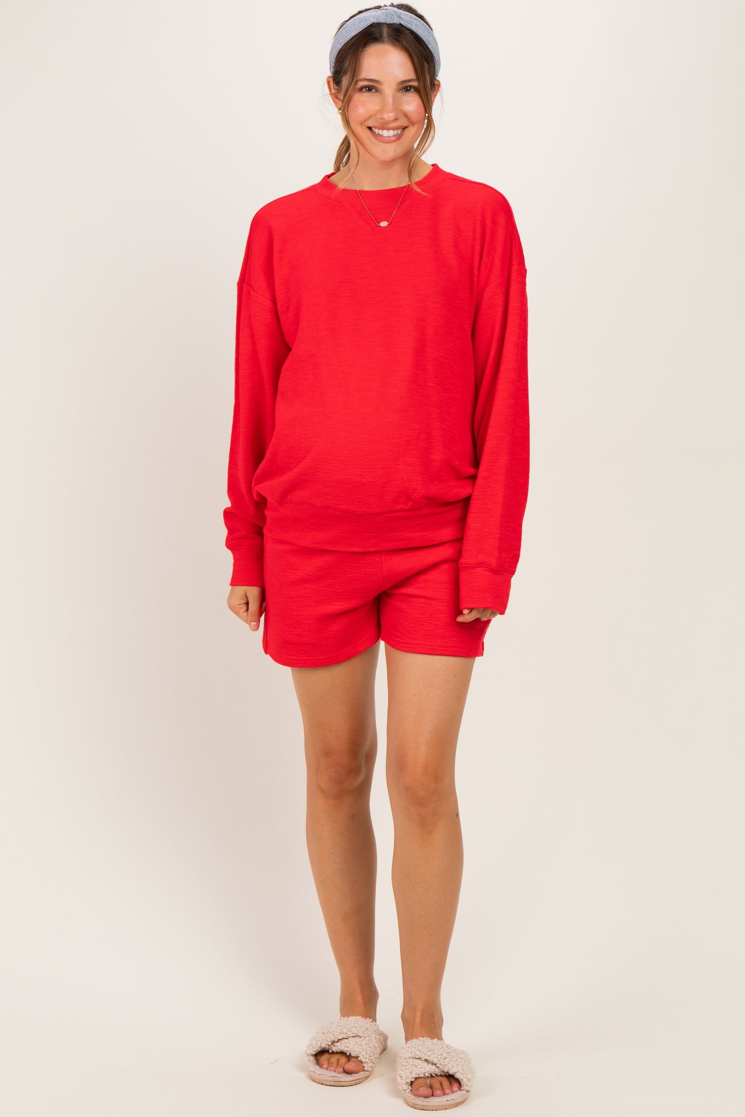 woman wearing a red maternity sweatshirt and matching shorts, smiling with a headband in her hair