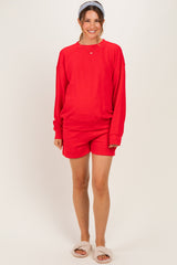 woman wearing a red maternity sweatshirt and matching shorts, smiling with a headband in her hair