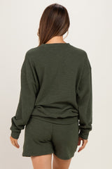 woman wearing a dark green maternity sweatshirt and matching shorts, seen from the back, showing a relaxed fit