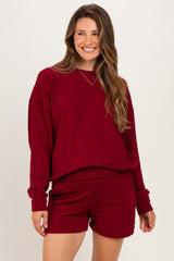 woman wearing a maroon maternity sweatshirt and matching shorts, smiling and styled casually