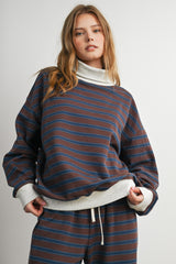 woman wearing a brown and blue striped oversized turtleneck sweatshirt with gray cuffs and matching bottom outfit