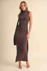 woman wearing a sleeveless brown maxi dress with a high neckline and a long scarf detail