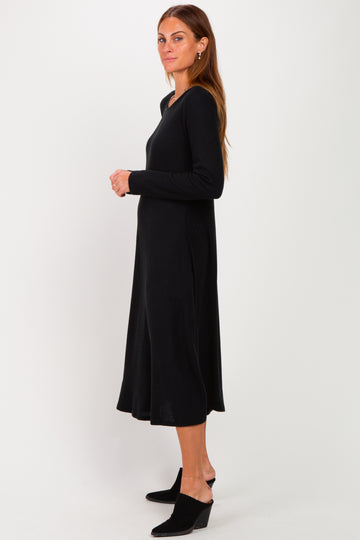 woman wearing a long black ribbed dress with a v-neck and a flared hem, standing sideways