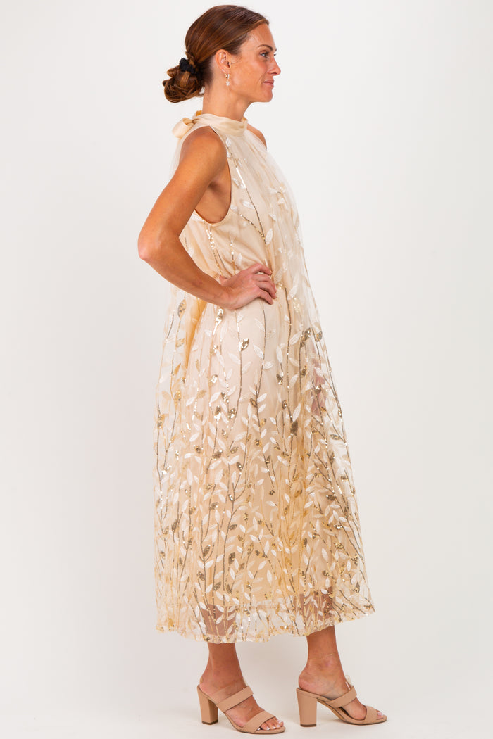 woman wearing a beige sleeveless dress with floral embroidery and a flowy silhouette, standing sideways