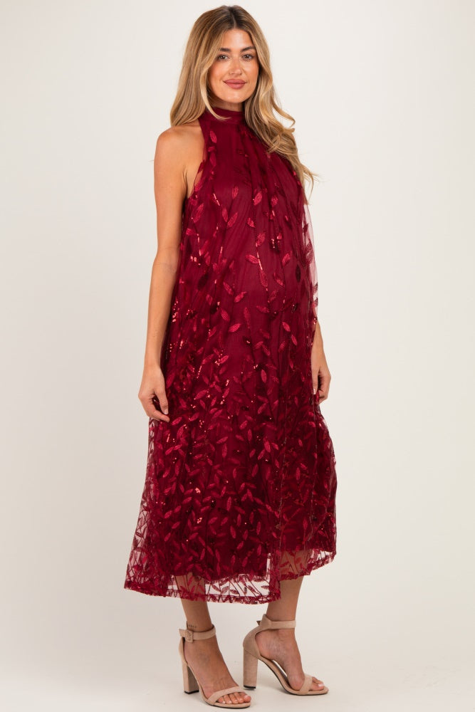 woman wearing a burgundy sleeveless maternity dress with floral embroidery and a flowing silhouette, showcasing her baby bump