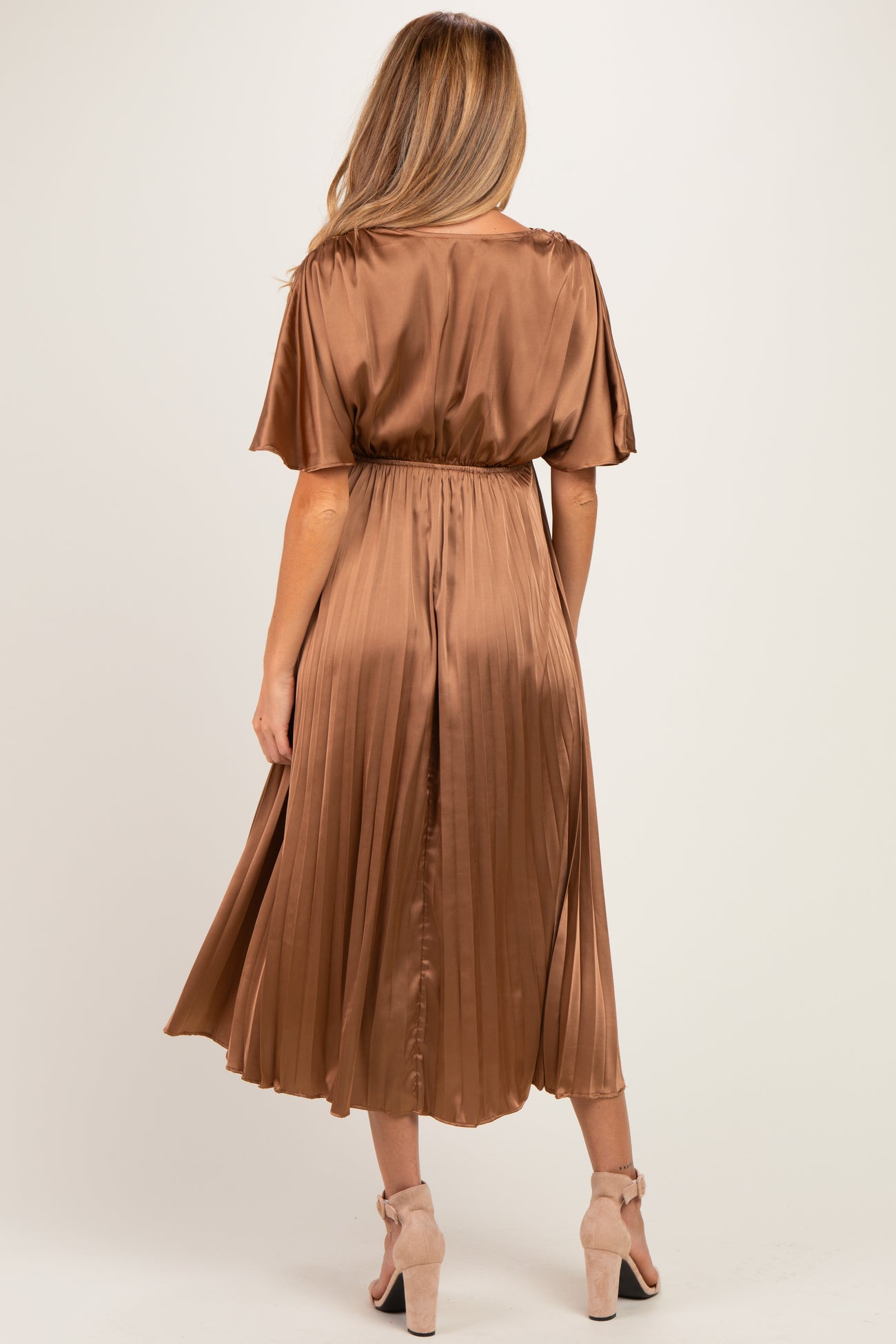 woman wearing a bronze satin pleated maternity dress with short sleeves and an elastic waist, showing the back view