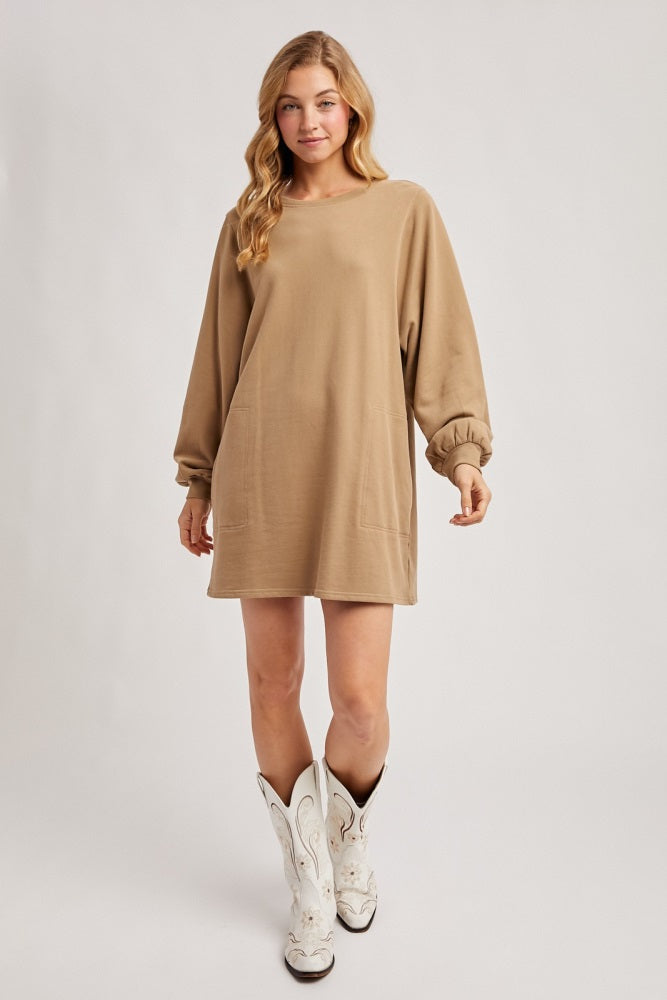 woman wearing a tan oversized sweatshirt dress with long sleeves and side pockets, paired with white cowboy boots