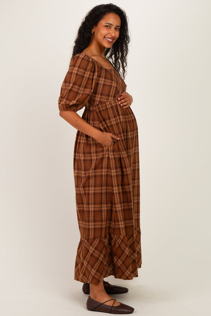 woman wearing a brown plaid maternity maxi dress with puff sleeves and a baby bump, smiling and posing with hands in pockets