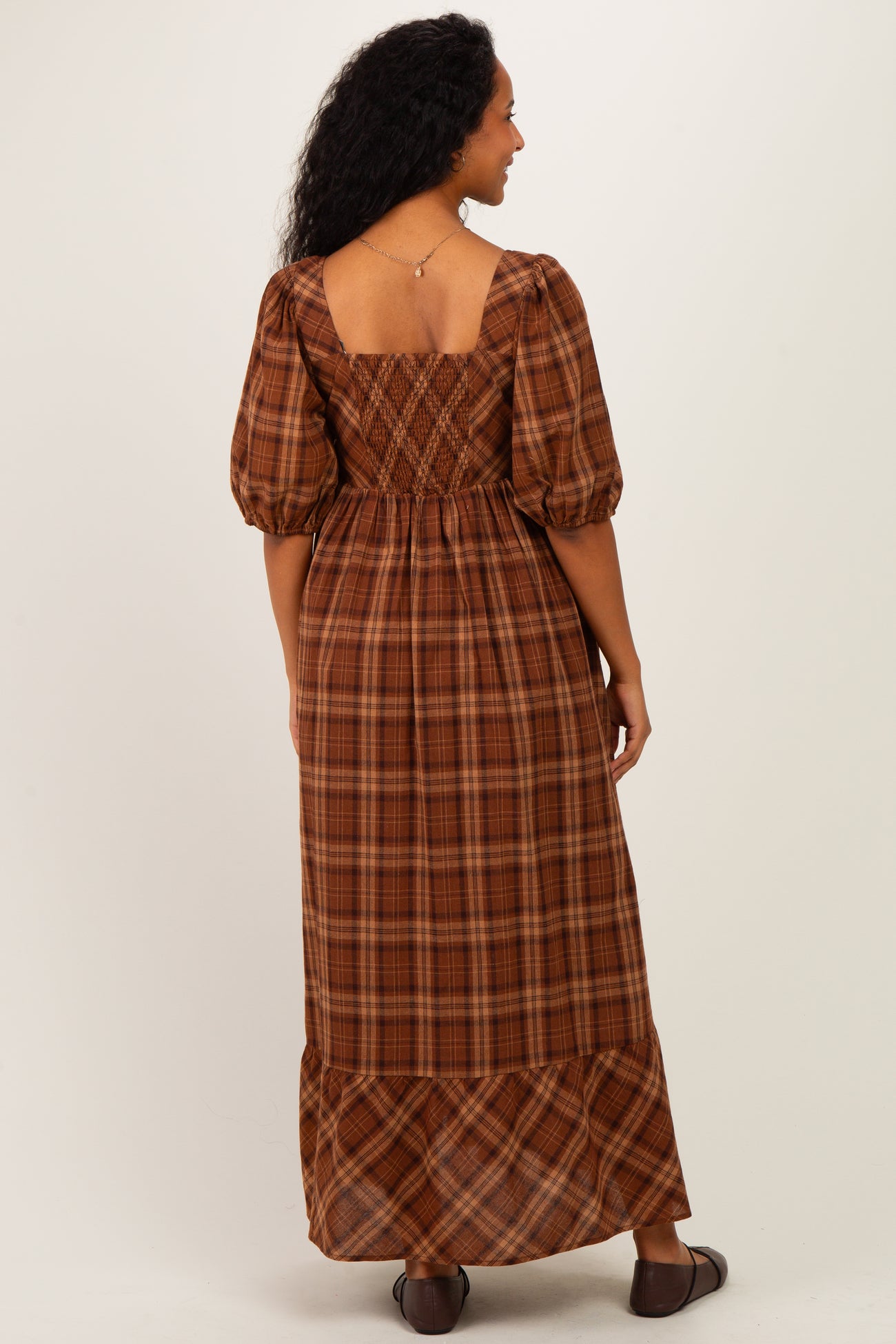 woman wearing a brown plaid maternity maxi dress with puff sleeves and a square back, showing off her baby bump