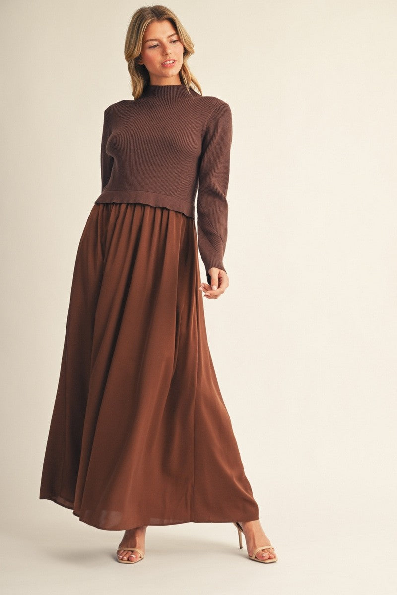 woman wearing a brown ribbed sweater and a flowing brown maxi skirt, standing elegantly against a neutral background
