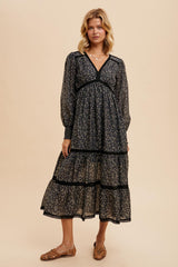 woman wearing a black floral tiered maxi dress with a v-neckline and long sleeves, standing on a neutral background