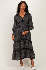 woman wearing a black floral maternity maxi dress with puff sleeves and a baby bump, smiling at the camera