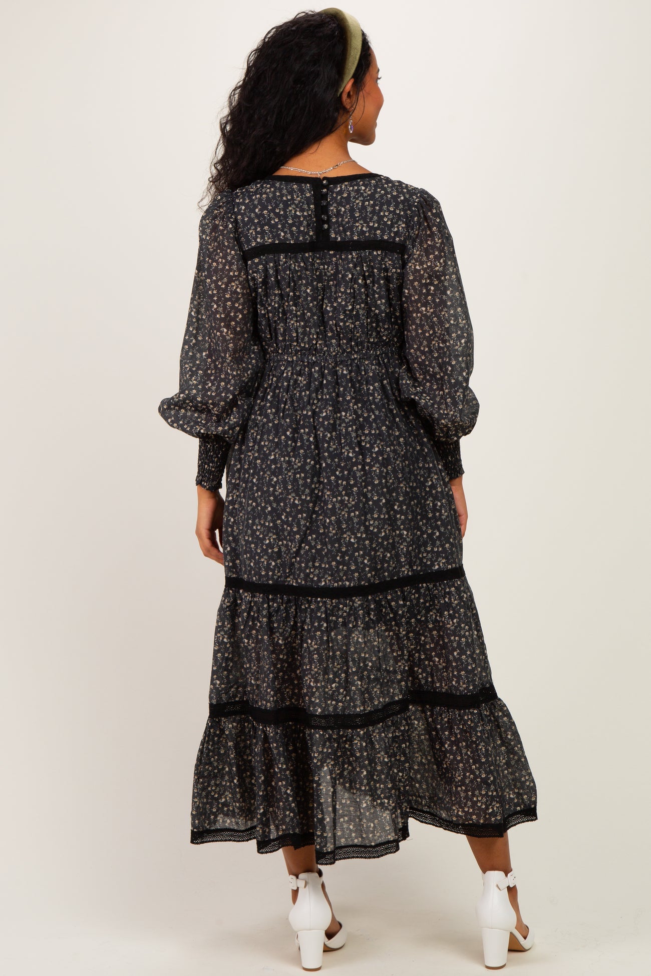 woman wearing a black floral maternity dress with long sleeves and tiered ruffles, showing a baby bump