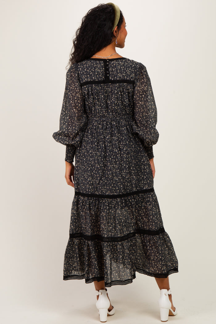 woman wearing a black floral maternity dress with long sleeves and tiered ruffles, showing a baby bump