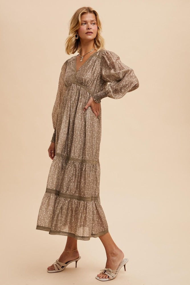 woman wearing a long beige floral maxi dress with puff sleeves and tiered skirt, posing with one hand on her hip