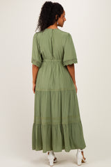 woman wearing a long green maternity dress with lace details and a tiered skirt, showing her baby bump from the back