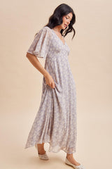woman wearing a lilac floral maxi dress with flutter sleeves and a v-neckline, standing on a light background