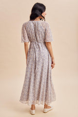 woman wearing a light purple floral maxi dress with short sleeves and a tie waist, seen from the back