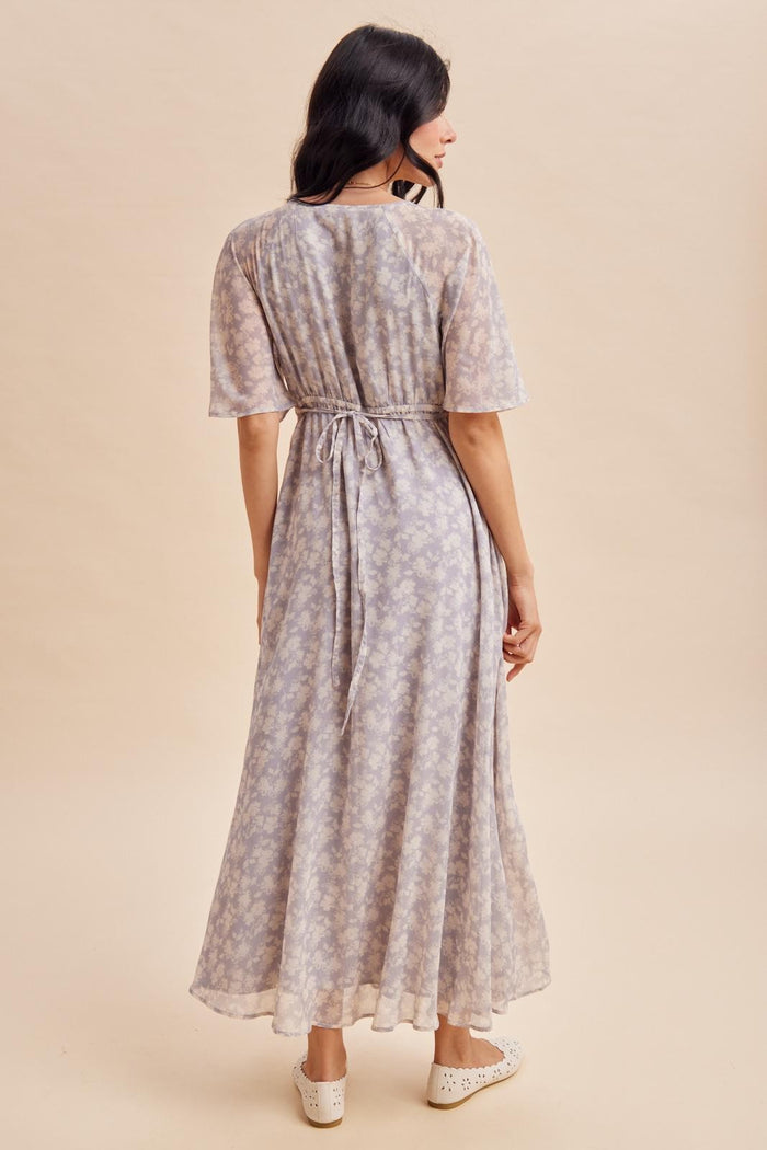 woman wearing a light purple floral maxi dress with short sleeves and a tie waist, seen from the back