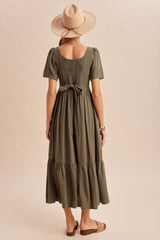 woman wearing an olive green midi dress with short puff sleeves and a tie belt, standing with her back to the camera
