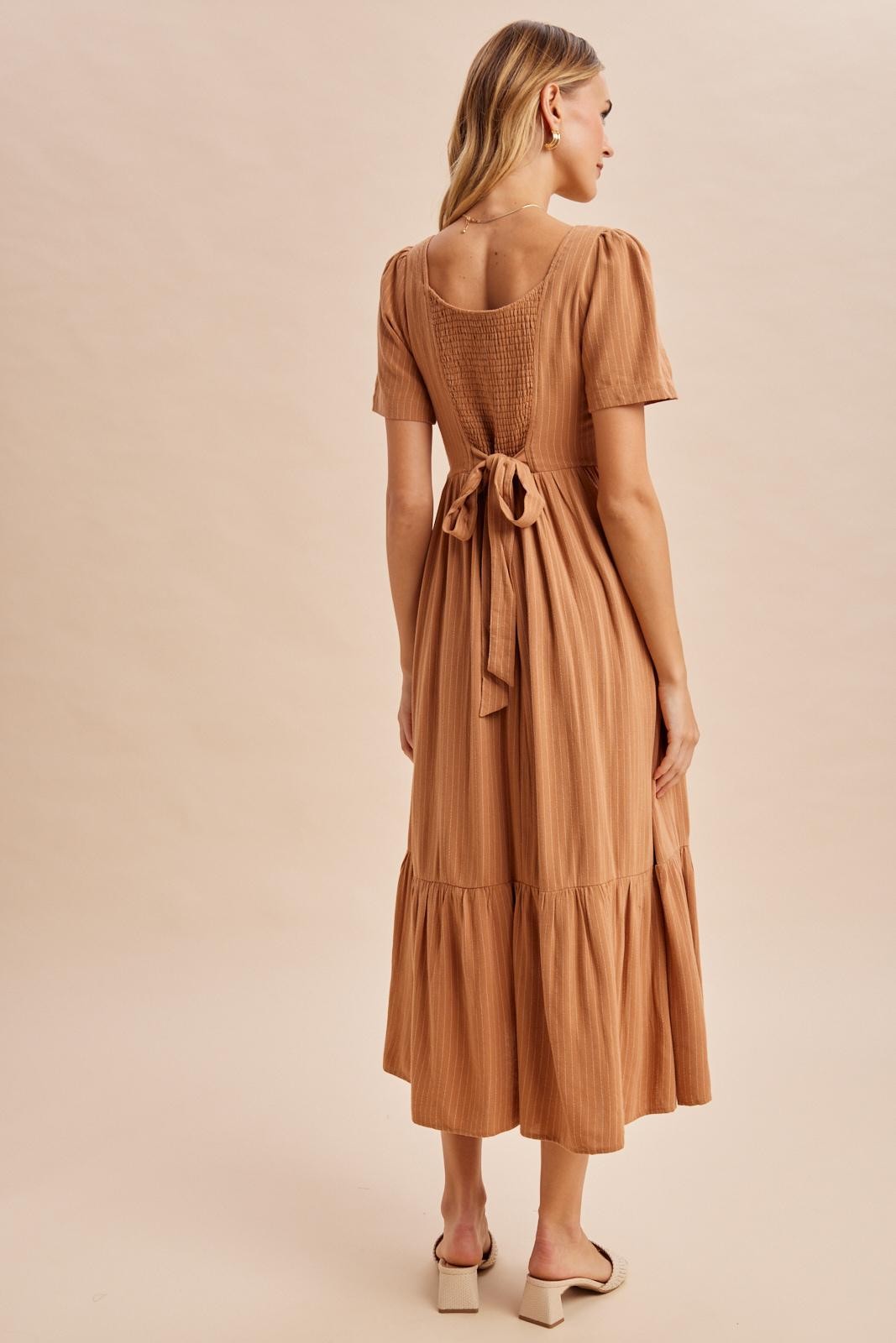 woman wearing a rust-colored short sleeve midi dress with a tied back detail and tiered skirt