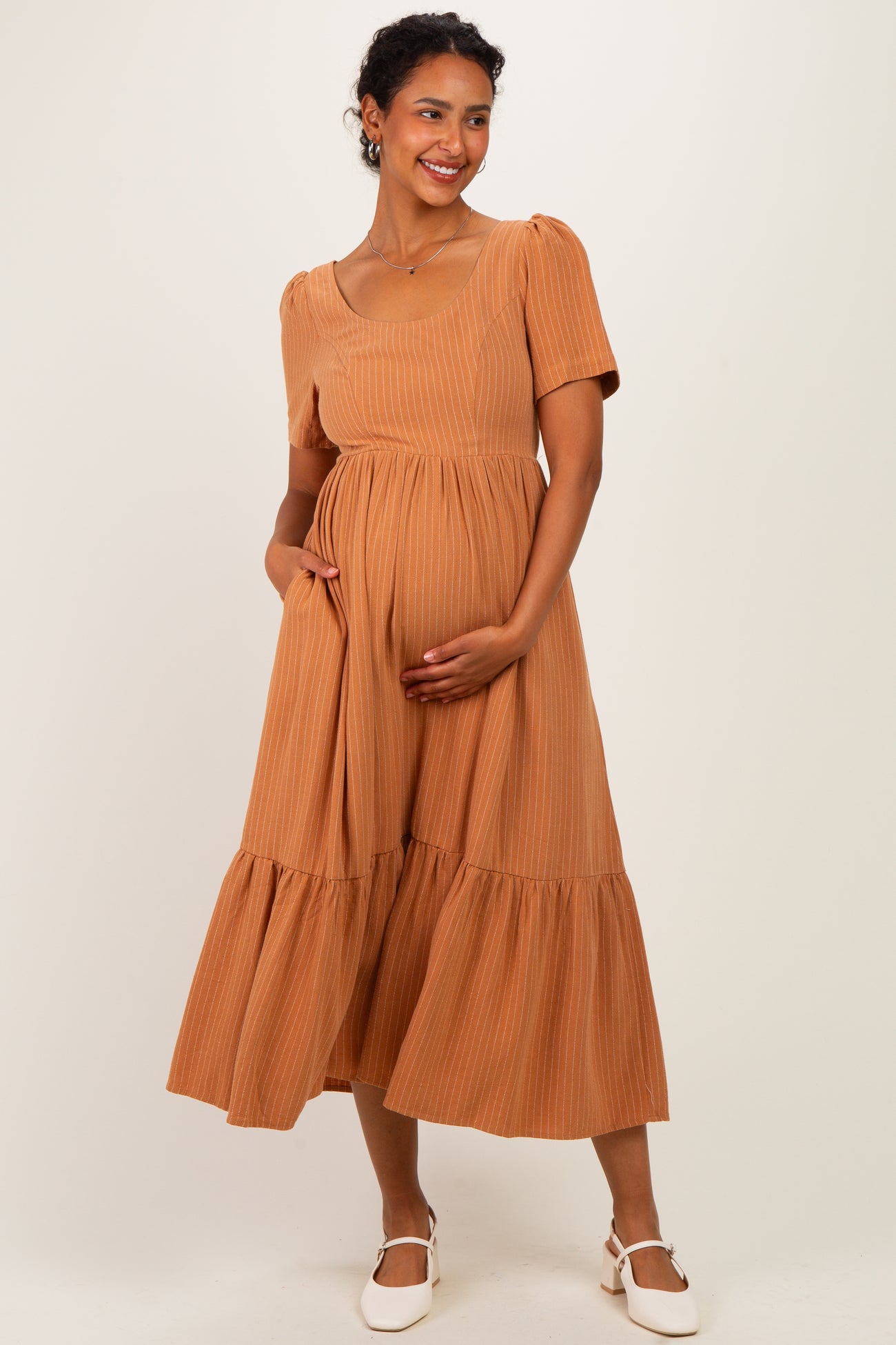 woman wearing a rust colored maternity dress with puff sleeves and a tiered skirt, gently cradling her baby bump