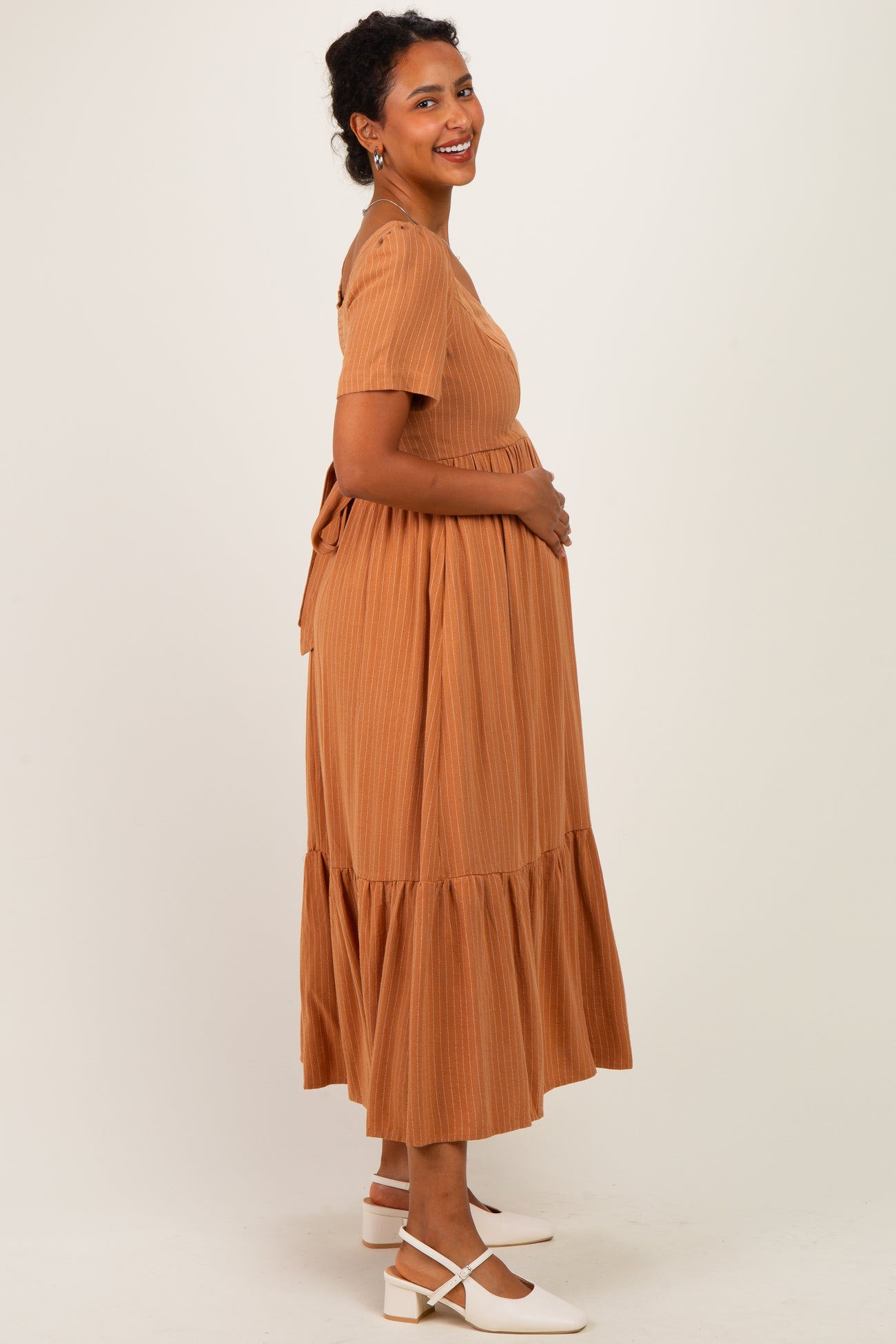 woman wearing a rust-colored maternity dress with short sleeves and a tiered skirt, holding her baby bump