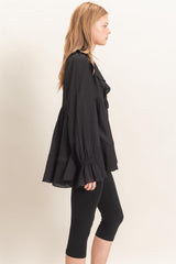 woman wearing a black pleated blouse with ruffled details and bell sleeves paired with black leggings
