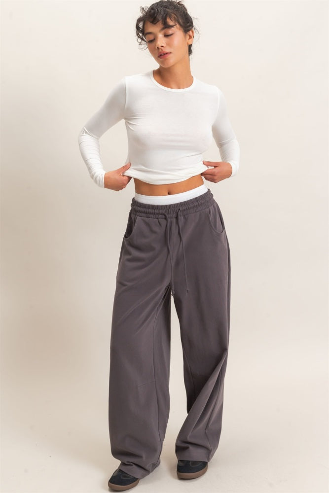 woman wearing a white long sleeve crop top and loose gray wide-leg pants, posing with hands on hips