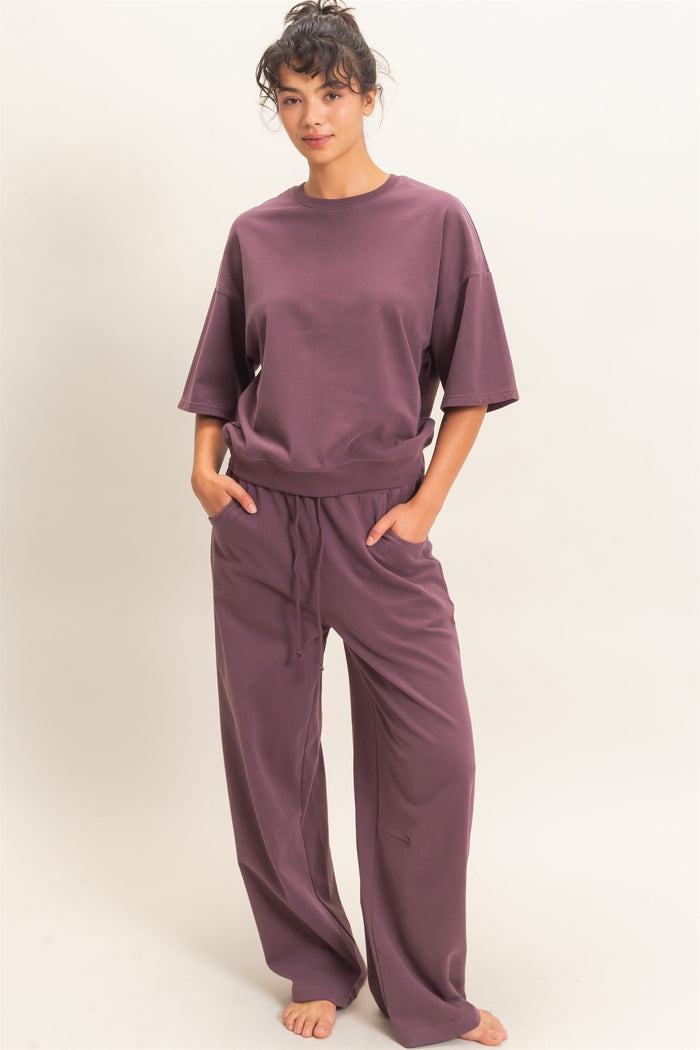 woman wearing a loose-fitting mauve t-shirt and matching wide-leg pants, standing with hands in pockets