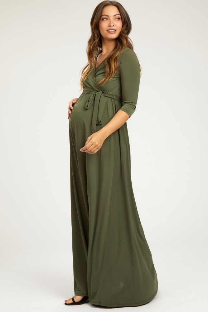 woman wearing a long olive green maternity dress with a wrap design and holding her baby bump